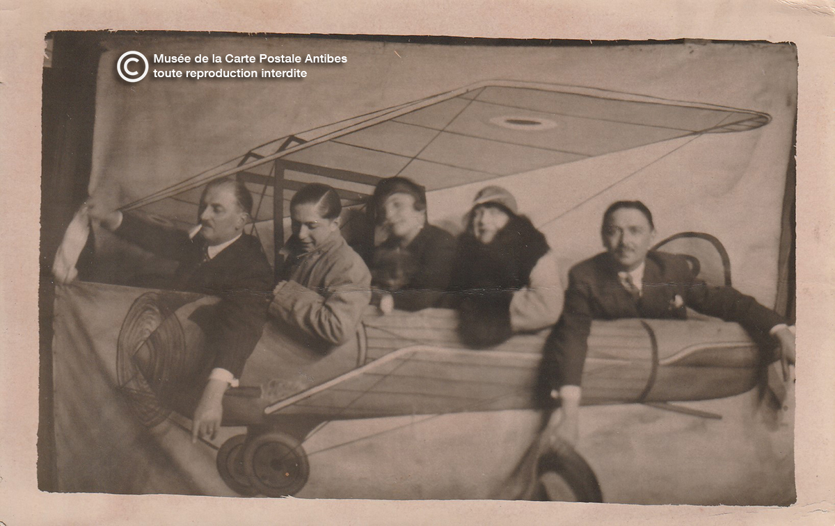 Carte postale Voyage en avion sans danger. Pilote et passagers dans un décor de photographe. Cliché très prisé à une époque où voyager en avion était assez exceptionnel. (Anonyme vers 1930).